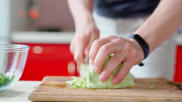 Male Hands with Knife Cuts Green Herbs on Wooden Cutboard on White Kitchen alt