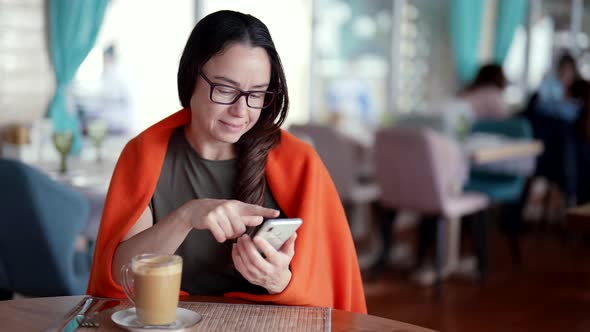 Middleaged Woman is Resting in Coffee Shop and Chatting Online By Smartphone Using Up App alt