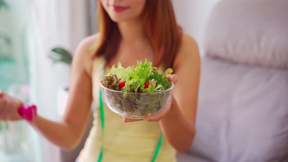 Young woman with homemade healthy salad exercising with dumbbell at home