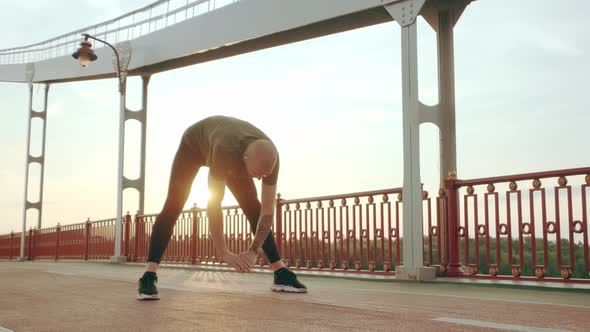 Young White Man in Black Sport Uniform Doing Warmup Before Run Pedestrian Bridge at Dawn alt