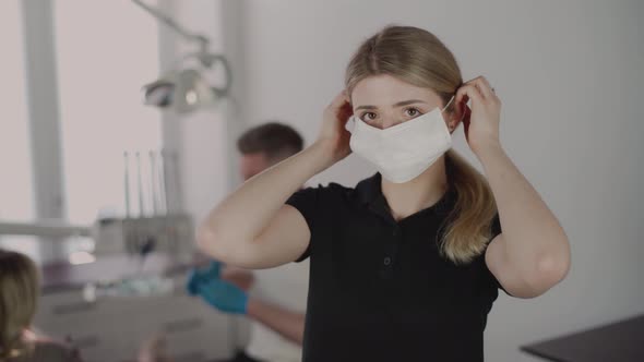 A female dentist puts on a protective mask and looks into the camera