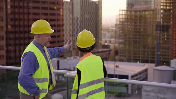 Two construction supervisors look out at city skyline from rooftop