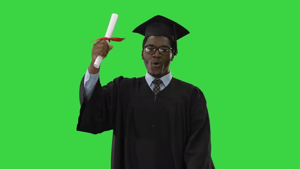 Happy African American Male Student in Graduation Robe Walking Towards Camera Waving His Diploma on alt