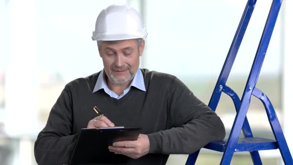Mature Worker with Helmet Writing on Clipboard alt