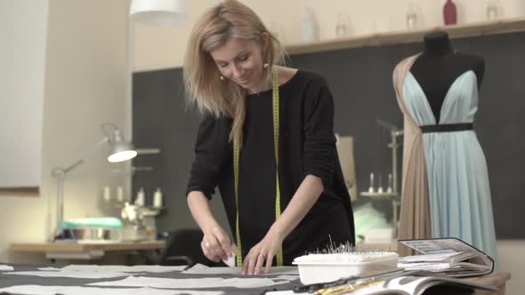 Blonde Caucasian Female in Black Dress with Tailor's Meter Around Neck Working with French Chalk alt