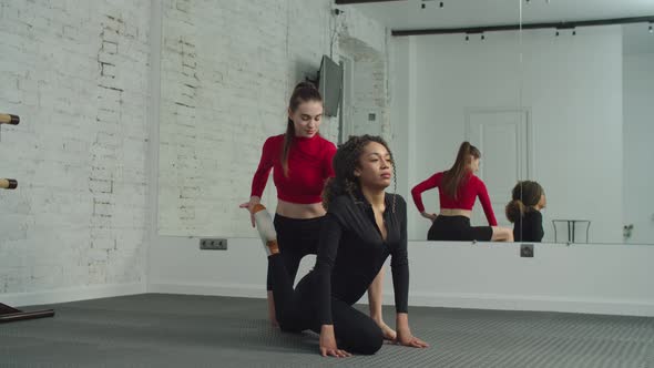 Yogi Trainer Helping Female to Do Pigeon Pose Indoors alt