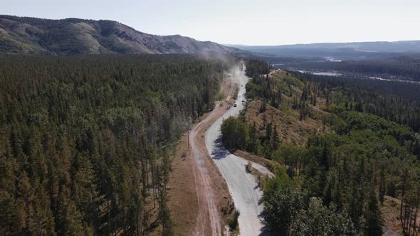 Multiple cars driving along a dusty logging road that leads through boreal forests near Ghost River, alt