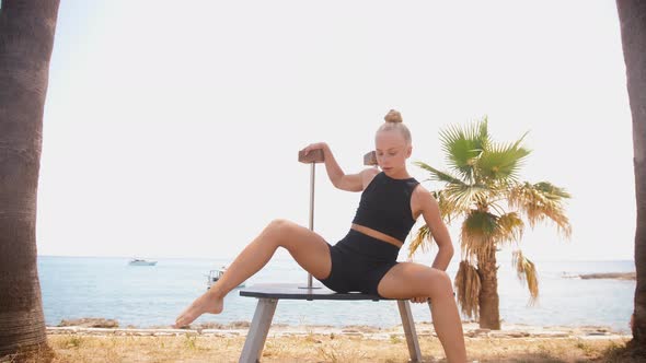 Young Blonde Female Gymnast Dancing By High Stands on the Beach alt