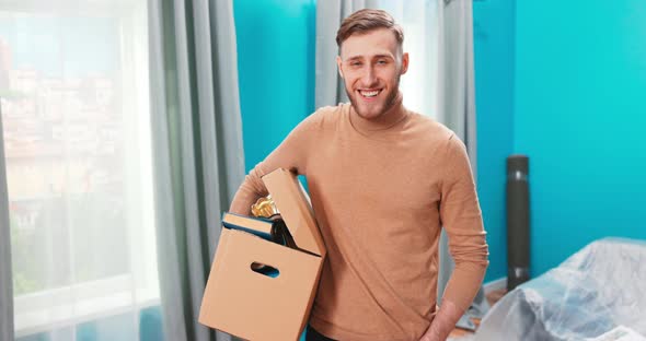 Portrait of Young Happy Man Standing in the Middle of New Apartment alt