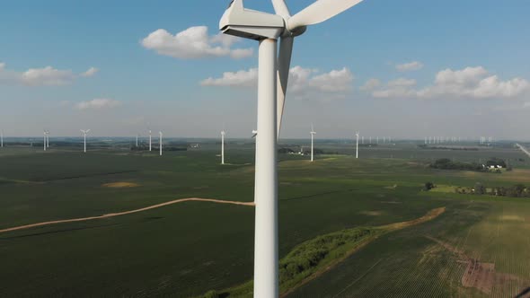 Flying up alongside a spinning wind generator in the middle of a field on a sunny summer day alt