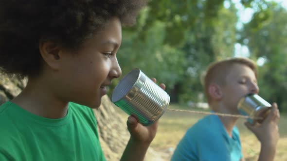 Black Male Teen Listening to Tin Can Phone Communicating With Friend, Kids Fun