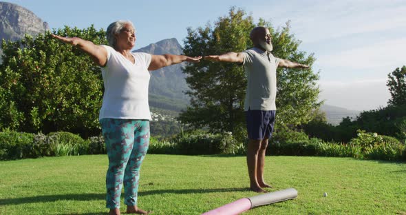 African american senior couple practicing yoga together while standing in the garden alt