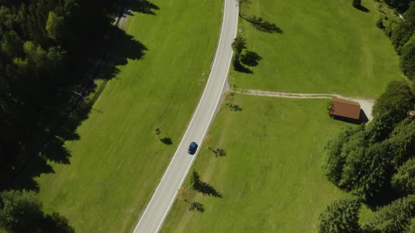 Sports car travelling through green fields and farmland in Germany, aerial view alt