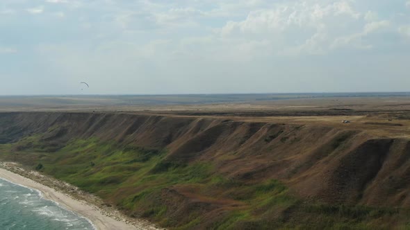 Stunning Aerial View on the Shoreline with Tall Hills and a Paraglider alt