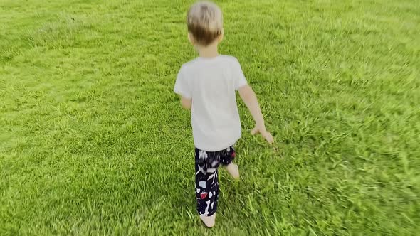 Happy Little Boy is Running on the Green Grass Field in the Park