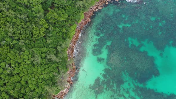 Aerial view of turquoise blue waters following coastline of green forest Praslin Seychelles