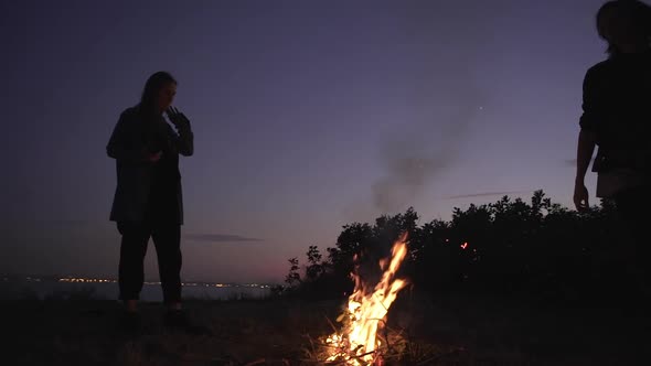 Young Multiethic Friends Staying Around Bonfire Warming Hands on Edge Over Sea Enjoying Magic Moment alt