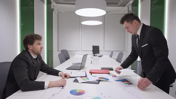 Side View of Angry Successful Businessman Throwing Paperwork Over Table to Manager Talking and alt