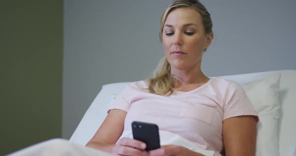 Caucasian female patient lying in hospital bed and using smartphone alt