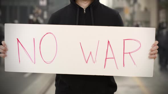 Unknown Activist Holds a Placard with NO WAR Text alt
