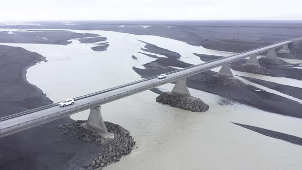 Aerial View of Cars Passing on a Bridge Road Running Through River in Iceland alt