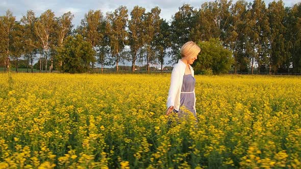 Attractive Young Blonde Woman Walks Through a Field of Rapeseed Smiling and Spinning Merrily