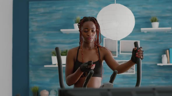 Slim Fit Trainer Wearing Sportswear Walking on Elliptical Bike Watching Aerobic Routine alt