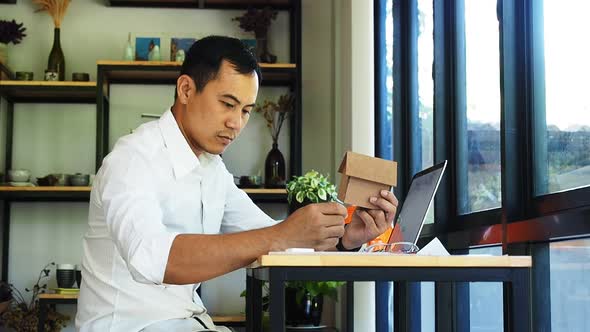 Architect is sitting in front of computer and holding small model of the house.