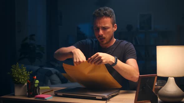 A Young Man Opens a Letter in the Living Room Late at Night and Enjoys the Result alt