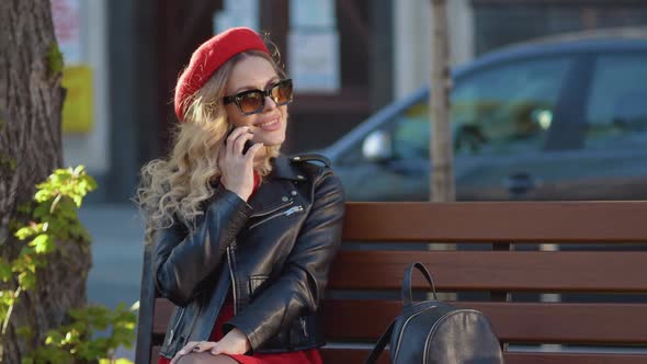 Young Beautiful Woman in a Red Beret and Dress Black Glasses and a Braid Sitting on a Park Bench alt