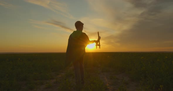 A Boy Is Standing on the Field and Playing with a Plane. Sunset.  alt
