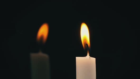 White Paraffin Candle with Yellow Tints Burns on Black Background in Reflection alt