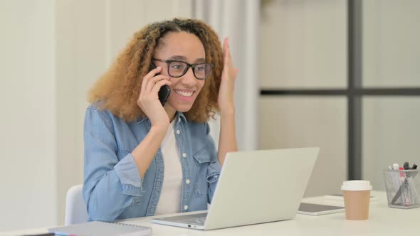 Angry African Woman Talking on Smartphone While Using Laptop alt