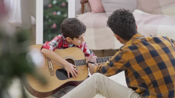 Portrait of Concentrated Boy Holding Guitar As Teenage Brother Teaching Him alt