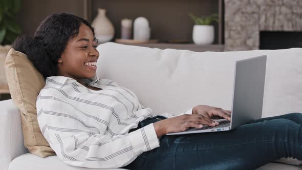 African Woman Lying on Sofa at Home Look at Laptop Screen Greeting Hello Make Video Call Talking alt
