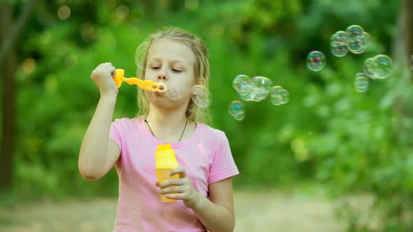 Portrait of funny lovely little girl blowing soap bubbles