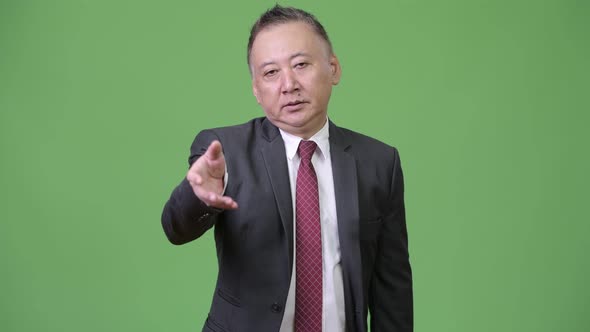 Mature Tired Japanese Businessman Giving Handshake Against Green Background alt