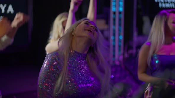 Joyful Carefree Blond Millennial Woman Dancing with Group of Friends in Night Club Lights alt