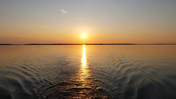 Calm lake water and bright sunset, view from drifting motor boat