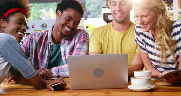 Group of friends using laptop while having cup of coffee alt
