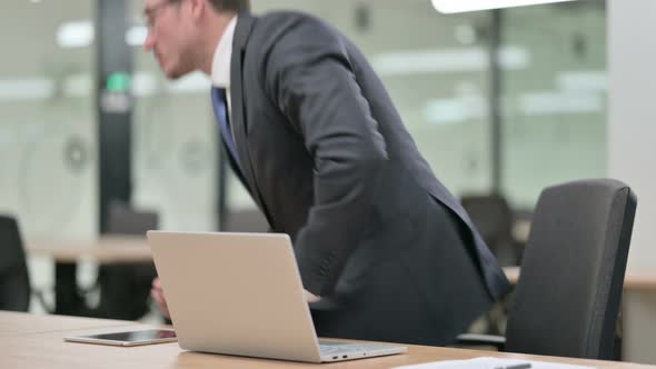 Middle Aged Businessman Standing Up and Going Away From Laptop in Office  alt