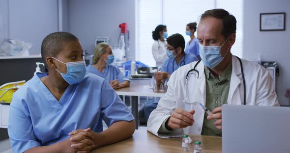 Diverse male and female doctor talking, man preparing covid vaccination, both wearing face masks alt