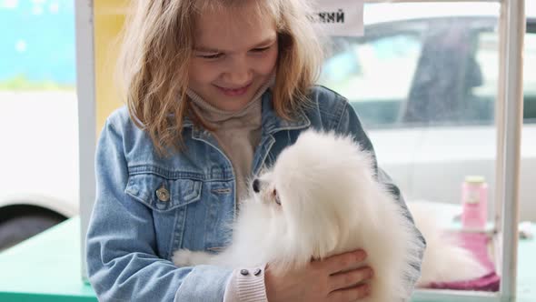 a Small and Happy Girl with a White and Fluffy Spitz Puppy alt