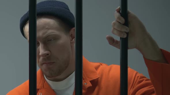 Caucasian Criminal Looking at Camera Through Prison Bars, Waiting for Judgment alt