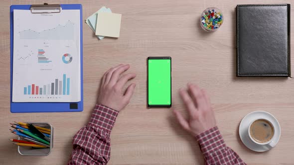 Top View of a Man's Hands Touch the Bottom Right Corner of a Green Screen on a Smart Phone alt