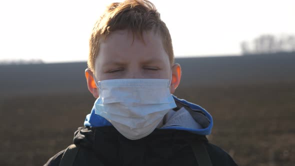 Portrait of Little Boy with Medical Face Mask Standing Outdoor. Sad Male Child Wearing Protective alt