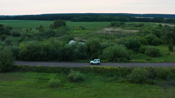 Aerial View of a Car Driving in Nature on a Field at Sunset alt