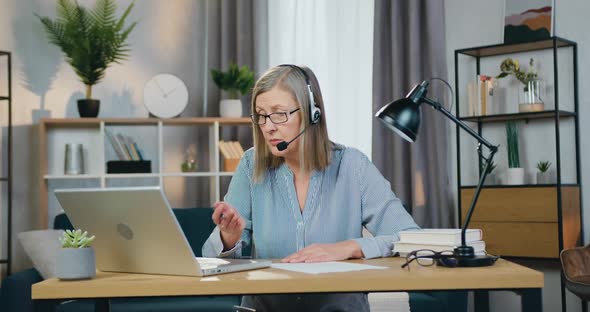 Aged Woman in Headset Having Video Conference on Laptop alt
