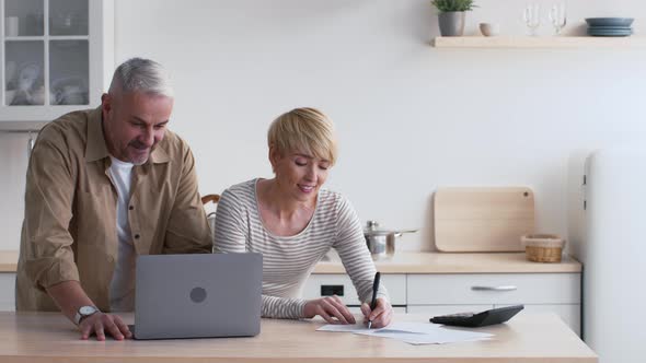 Happy MiddleAged Spouses Calculating House Expenses And Bills At Home alt