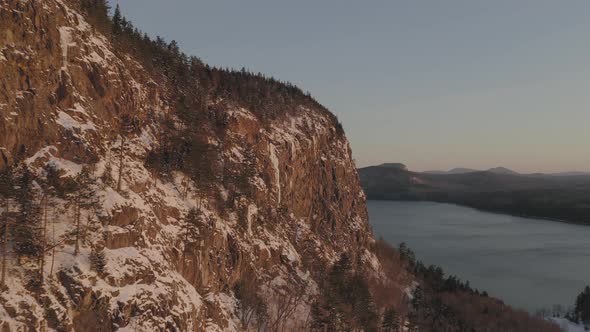 Flying towards a giant icicle on the side of a snow dusted cliff at dawn AERIAL alt